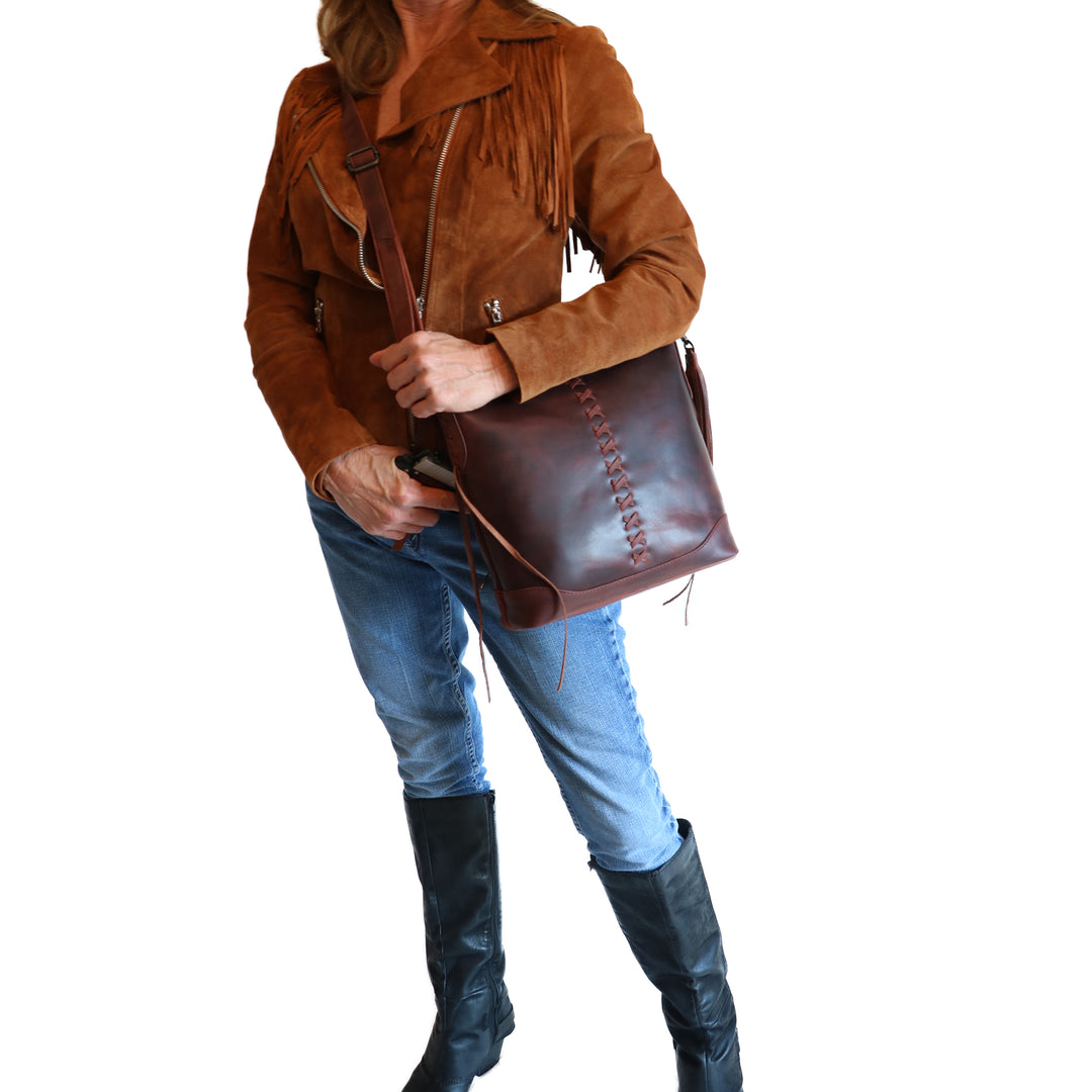 Model wearing Style "Blake" | Concealed Carry Crossbody with Criss-Cross Stitching and removable tassel accents | Dark Mahogany Full-Grain Leather | By Lady Conceal