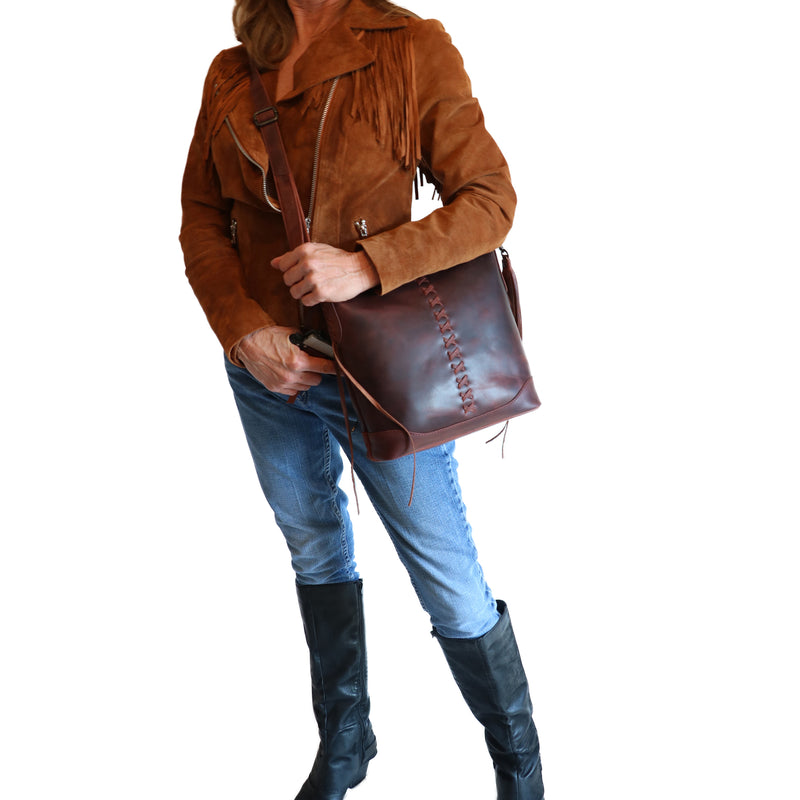 Model wearing Style "Blake" | Concealed Carry Crossbody with Criss-Cross Stitching and removable tassel accents | Dark Mahogany Full-Grain Leather | By Lady Conceal